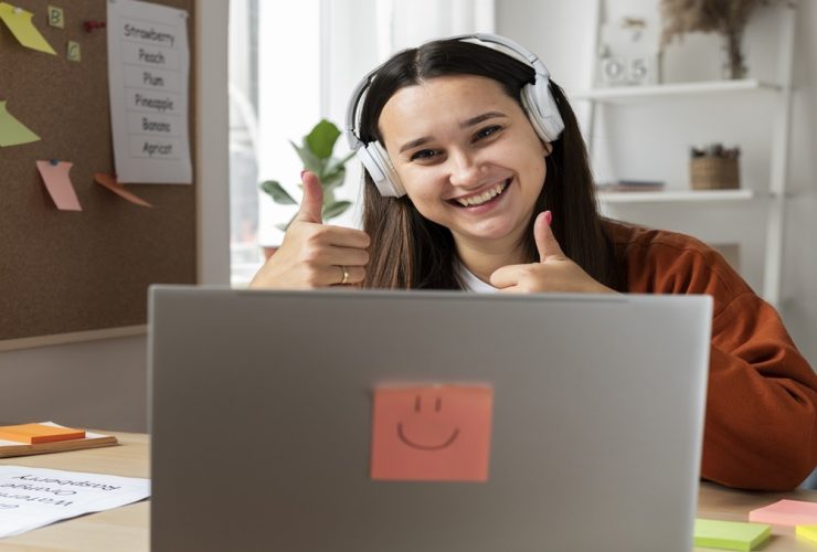 Pessoa sorridente usando fones de ouvido, com dois polegares erguidos diante de laptop